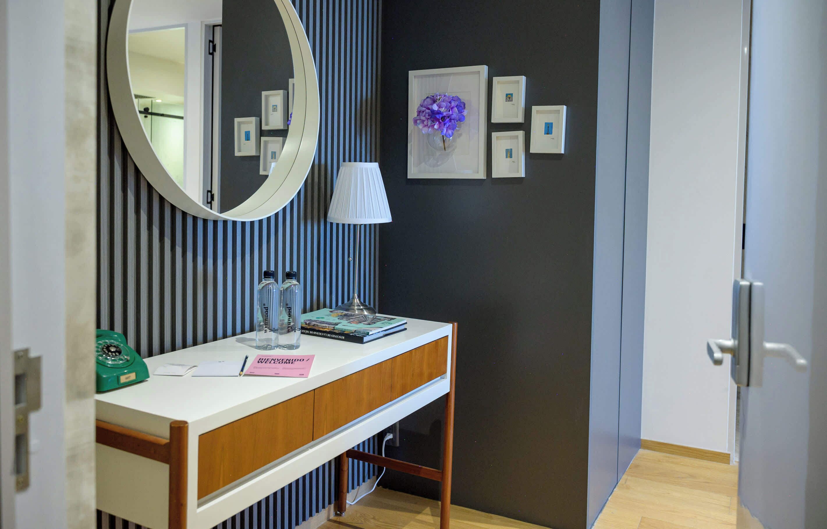 A modern bathroom with a white vanity, a round mirror, a green rotary phone, and a vase with purple flowers.