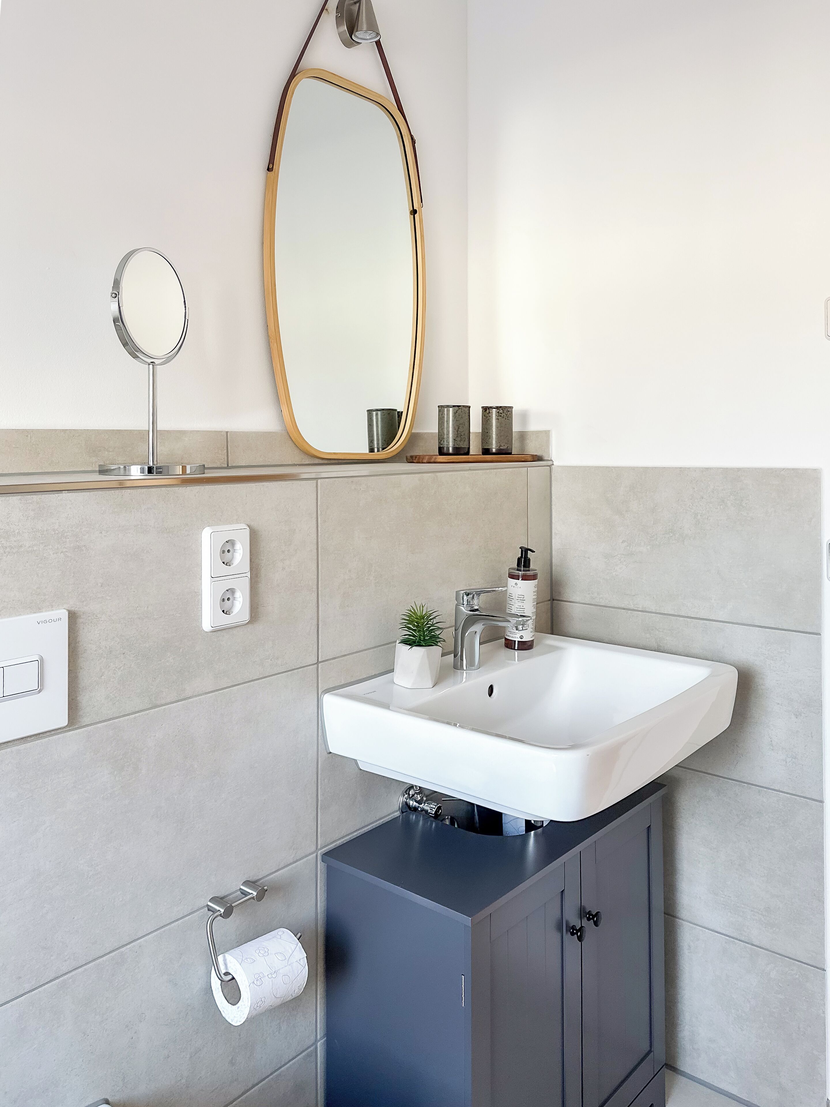 A modern bathroom with a white sink, a large mirror, and a cabinet below.