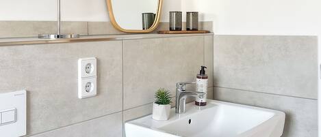 A modern bathroom with a white sink, a large mirror, and a cabinet below.