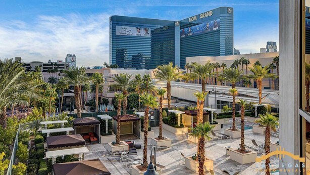 Un patio de hotel con palmeras, mobiliario exterior y vista al hotel MGM Grand al fondo.