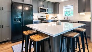 A modern kitchen with grey cabinets, a black refrigerator, a large island with stools, and pendant lighting. - Family Retreat in Birmingham – 7BR/4BA (Birmingham)