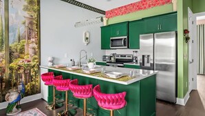 A modern kitchen with green cabinets, a central island with bar stools, a stainless steel refrigerator, and a decorative mural on the wall.