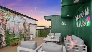 A rooftop patio with outdoor seating, a mural, and a neon sign.