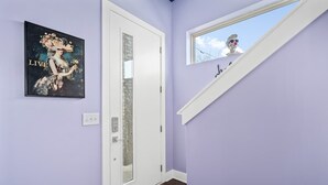 Ein Flur mit lila Wand, einer weißen Tür, einem Bilderrahmen, einem Fenster und einer kleinen Statue.