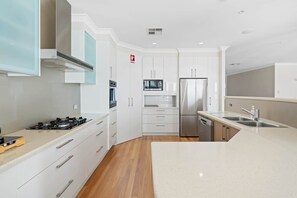 A modern kitchen with white cabinetry, stainless steel appliances, and a wooden floor. - Serene by Coast Hosting (Point Clare)