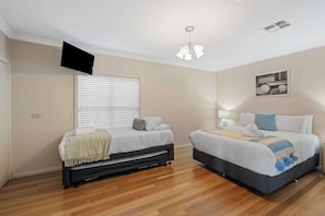 A bedroom with two beds, a ceiling fan, a mounted TV, and a window with blinds.