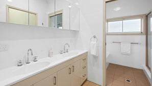 A modern bathroom with two sinks, a mirror, and a shower area. - Absolute Waterfront. Pool. Heated Spa. Sleeps 10 (Point Clare)