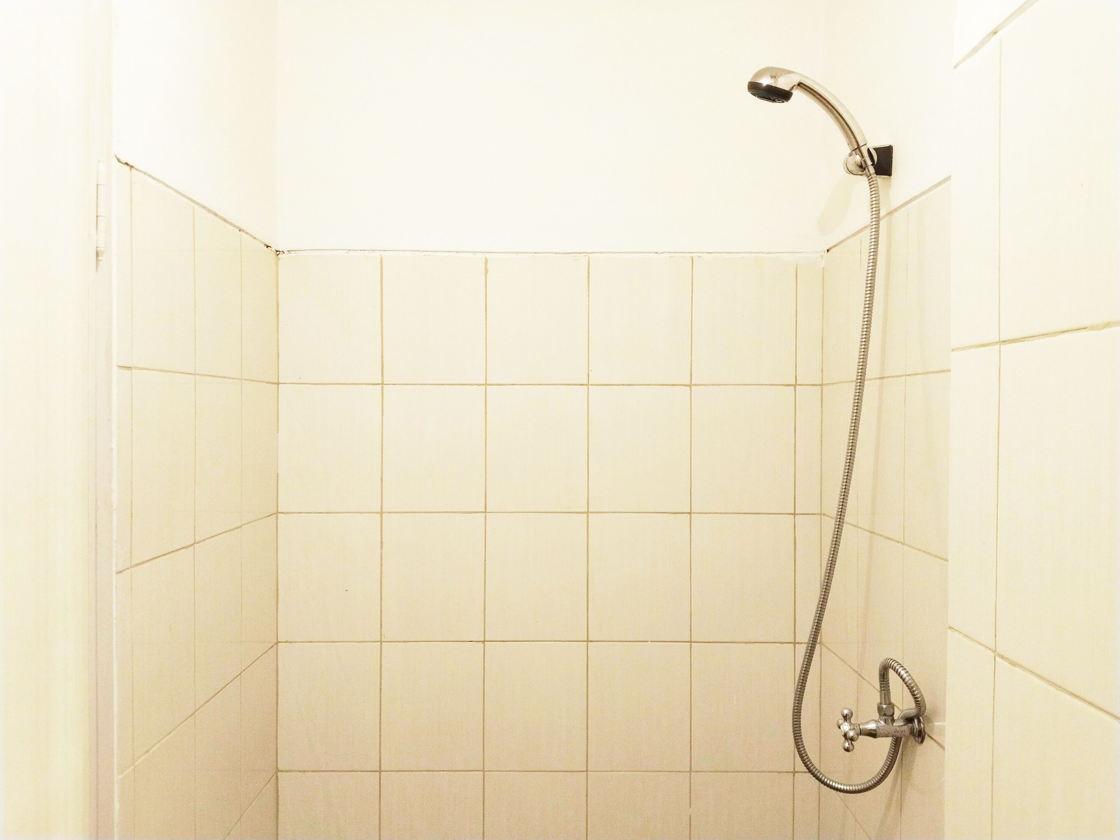 Una doccia con soffione a mano e rubinetto a muro in una stanza rivestita di piastrelle.