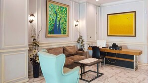 Un salon moderne avec un canapé, une table basse et un bureau avec un ordinateur. Il y a deux lampes fixées au mur et un tableau représentant un arbre.