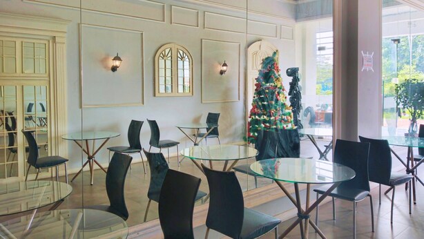 Un espace de restauration moderne avec des tables en verre et des chaises noires, un sapin de Noël et une vue sur l’extérieur.