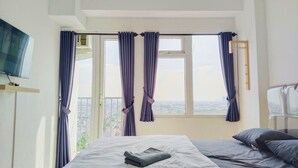 Une chambre d’hôtel avec un lit, un téléviseur fixé au mur et une fenêtre avec des rideaux.