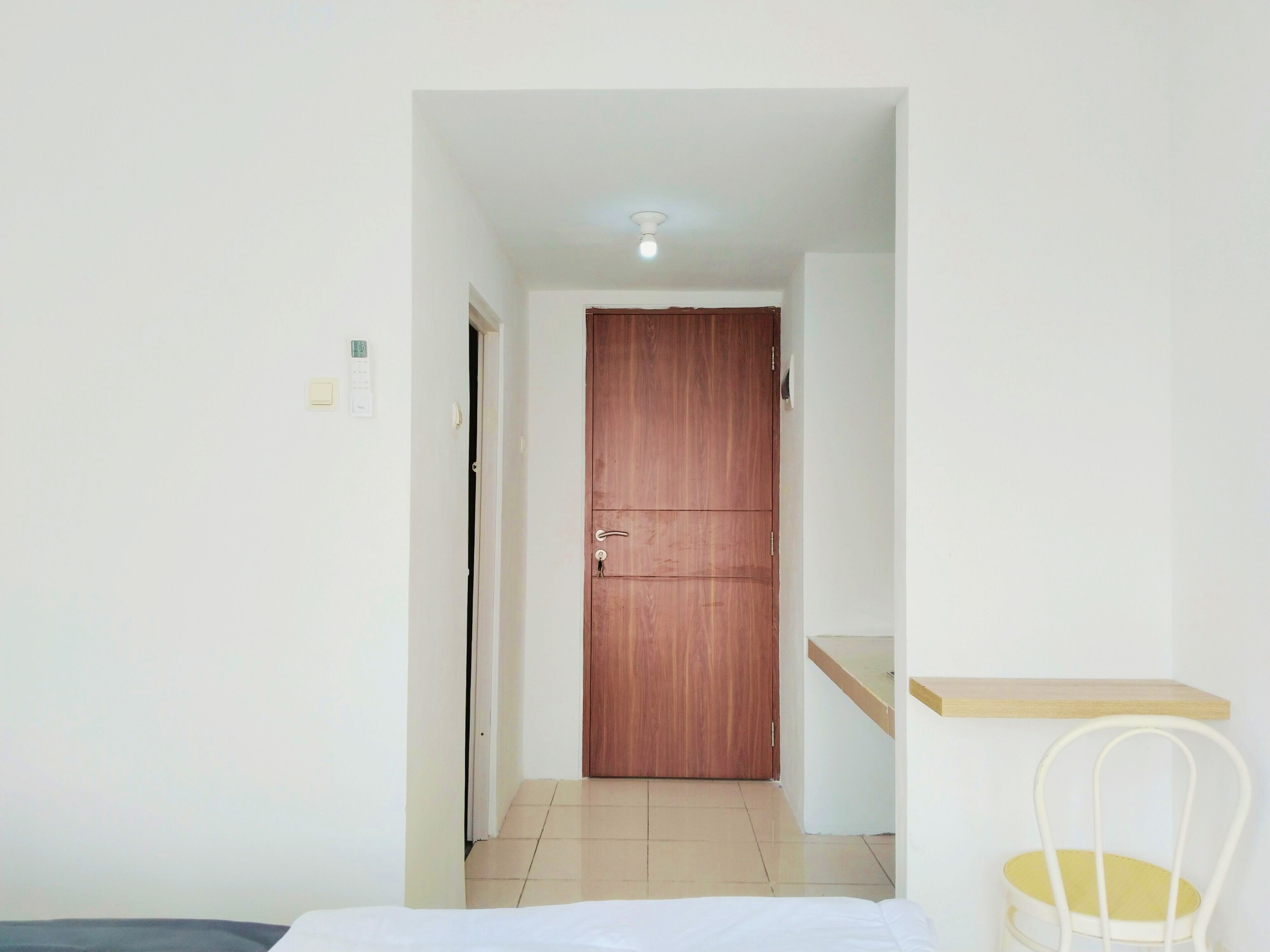 A hotel room with a wooden door, a bed, a chair, and a small shelf.