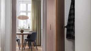 Un pasillo con piso de madera que conduce a un comedor con mesa y sillas, una lámpara colgante y vistas a una ventana con cortinas.