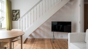 Eine Treppe mit weißen Geländern, ein an der Wand befestigter Flachbildfernseher, ein Holzes Esstisch und ein weißes Sofa.