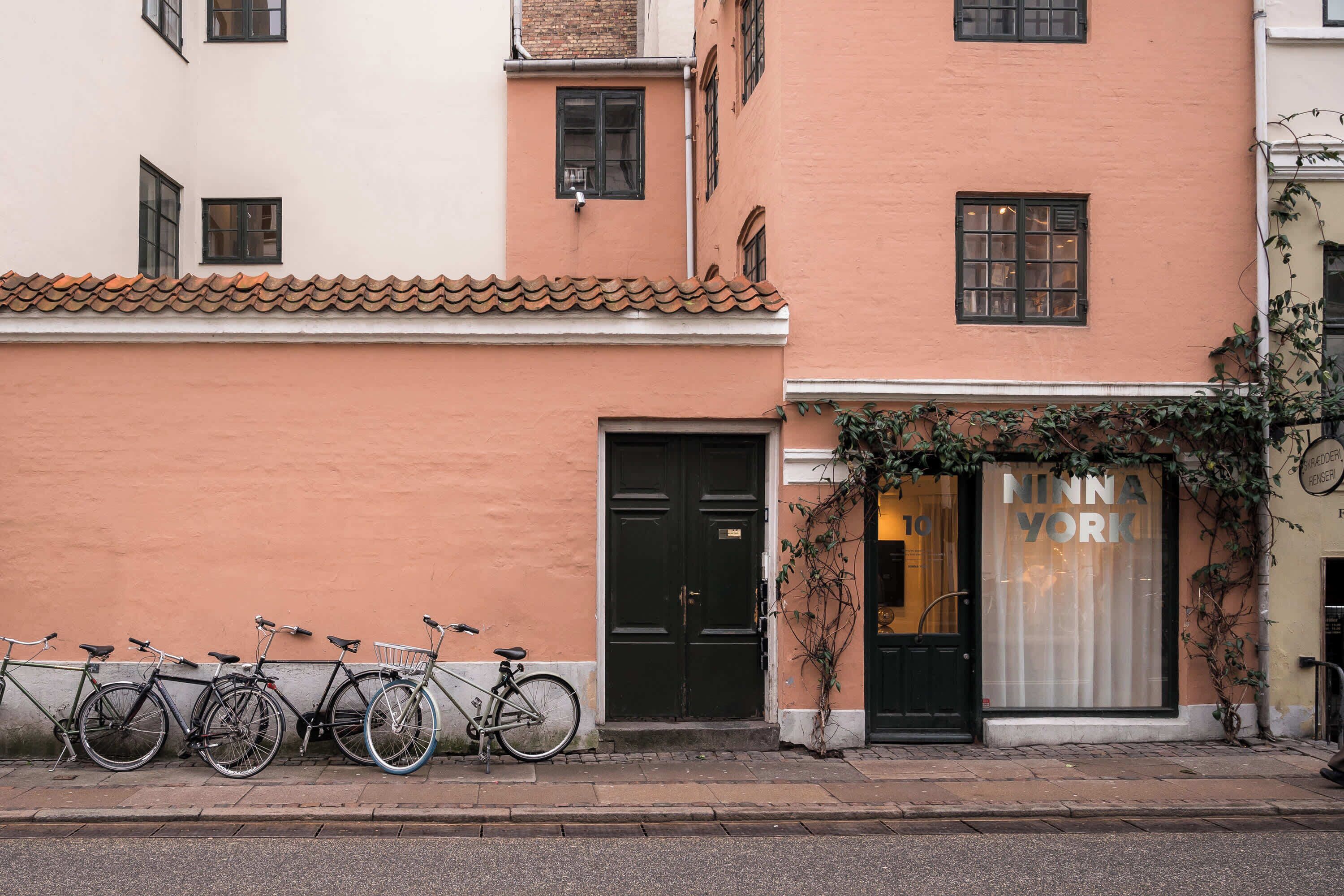 A row of bicycles parked against a building with a black door and a shop window with the sign "MINNA YORK".