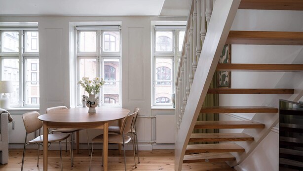 Ein Essbereich mit einem runden Holztisch und Stühlen, einer Vase mit Blumen sowie einer Treppe mit Holzstufen.