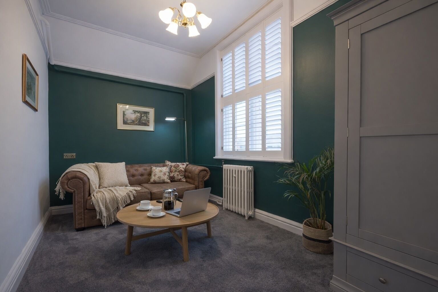 Een gezellige woonkamer met een bruine leren bank, een ronde salontafel en een groot raam met luiken.
