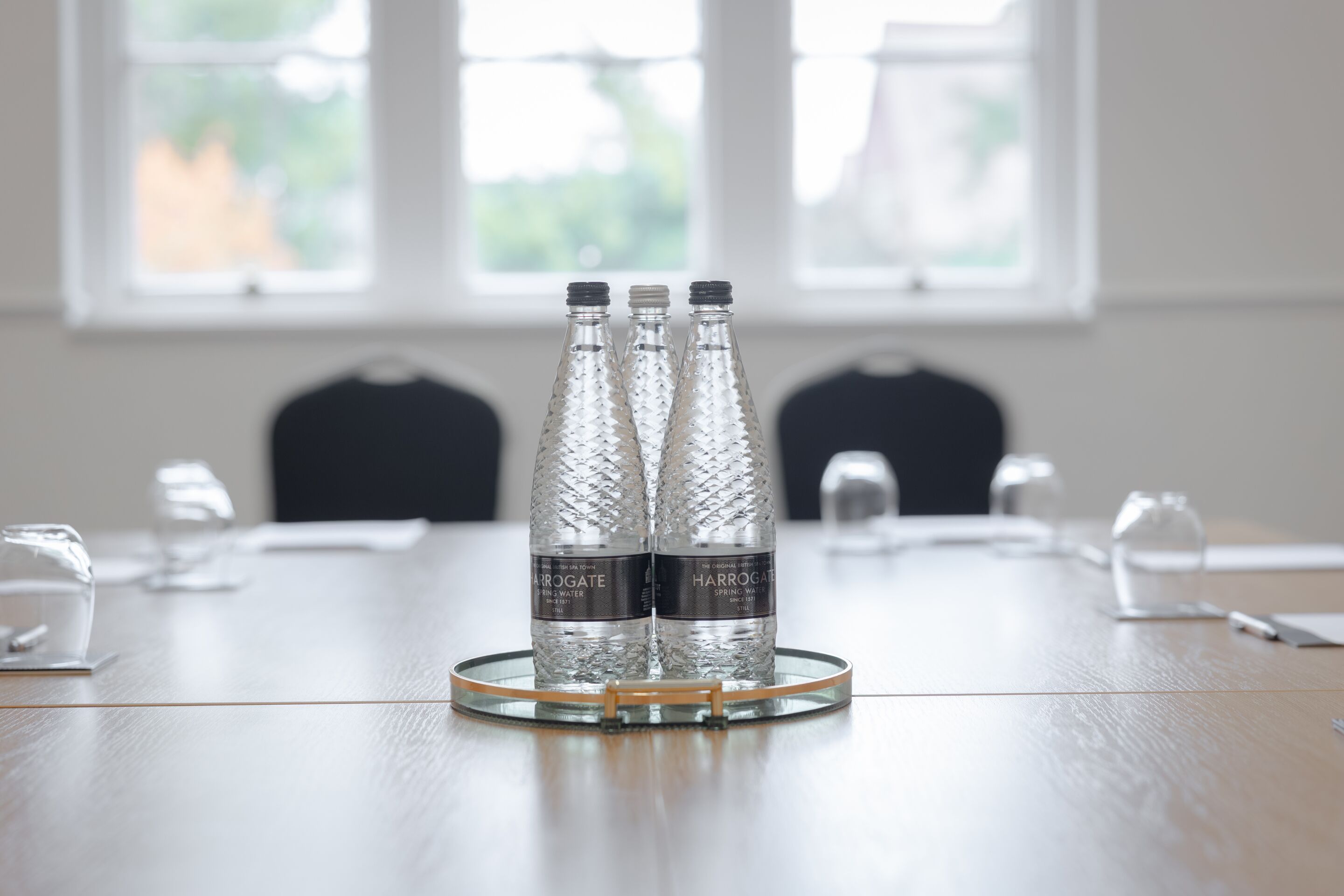Una mesa de conferencias con tres botellas de agua con la etiqueta "Harrogate Spring Water" y una jarra de cristal.