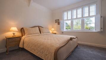 A bedroom with a bed, two bedside tables with lamps, a window with shutters, and a framed picture on the wall.