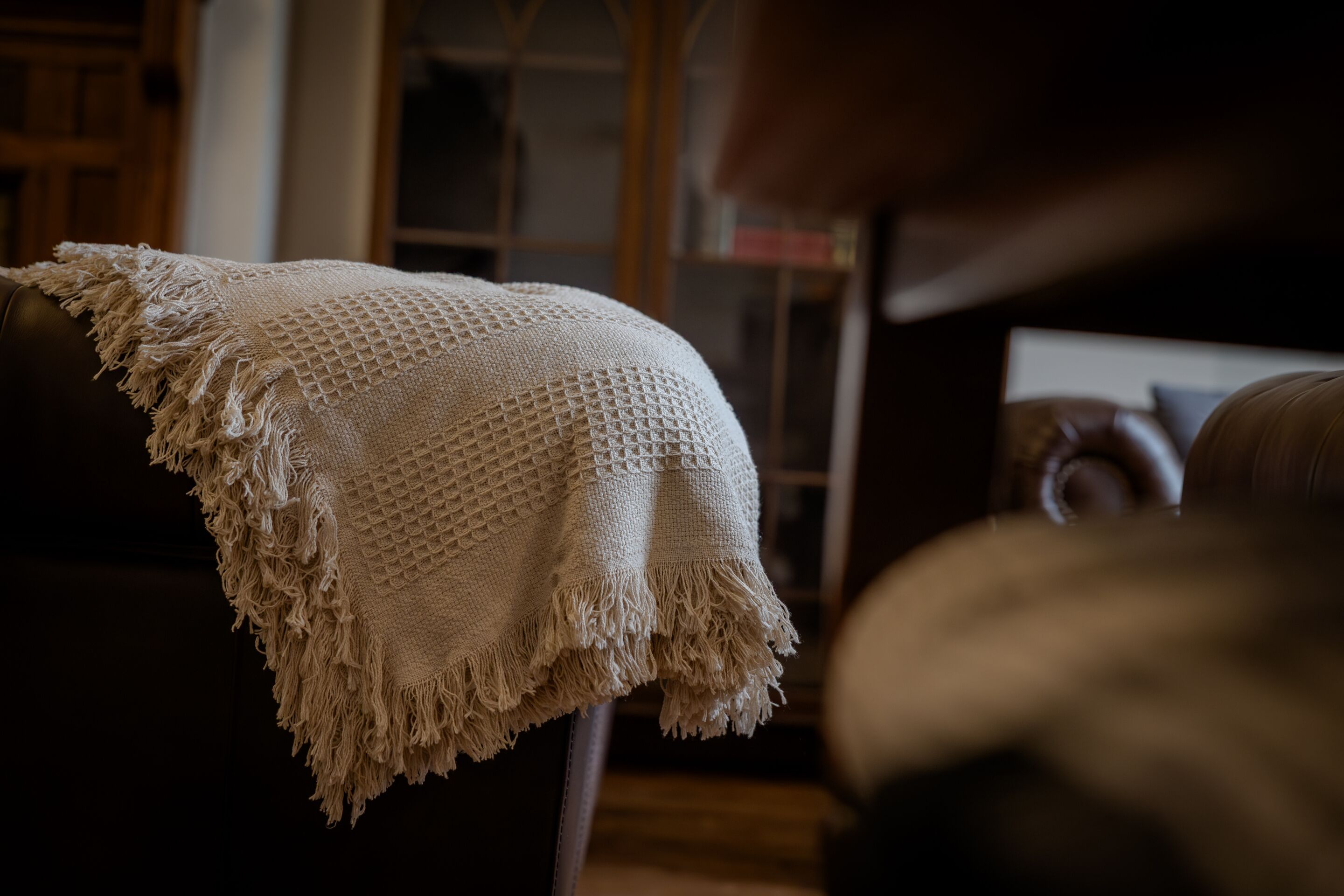 Un salon chaleureux avec un grand plaid texturé drapé sur un fauteuil en cuir.