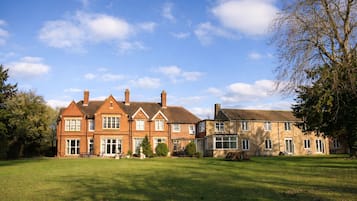 A large, traditional brick house with multiple chimneys, a well-maintained lawn, and a clear blue sky.