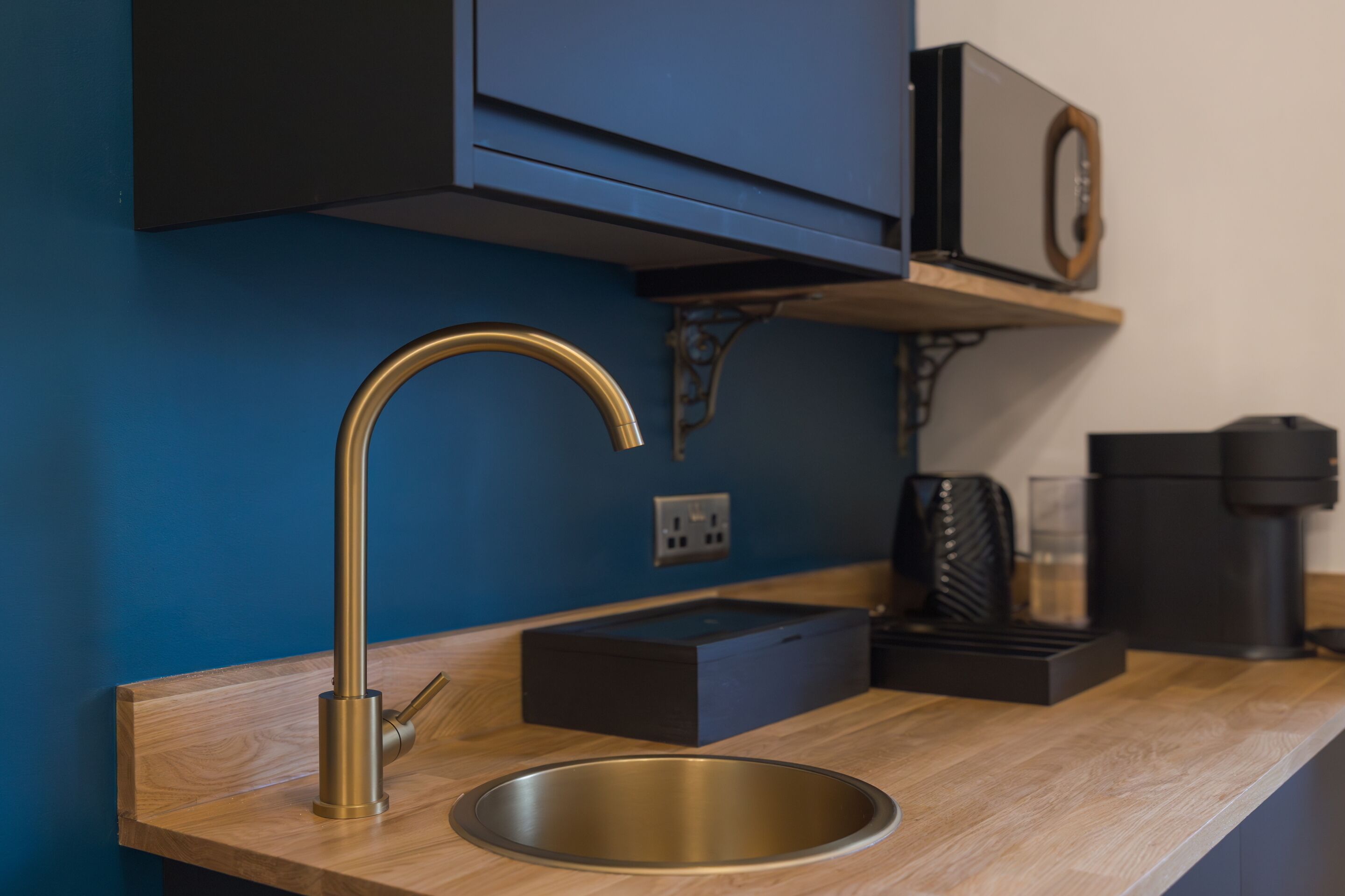 A kitchen with a stainless steel sink, a gold faucet, a coffee maker, and a microwave on a wooden countertop.