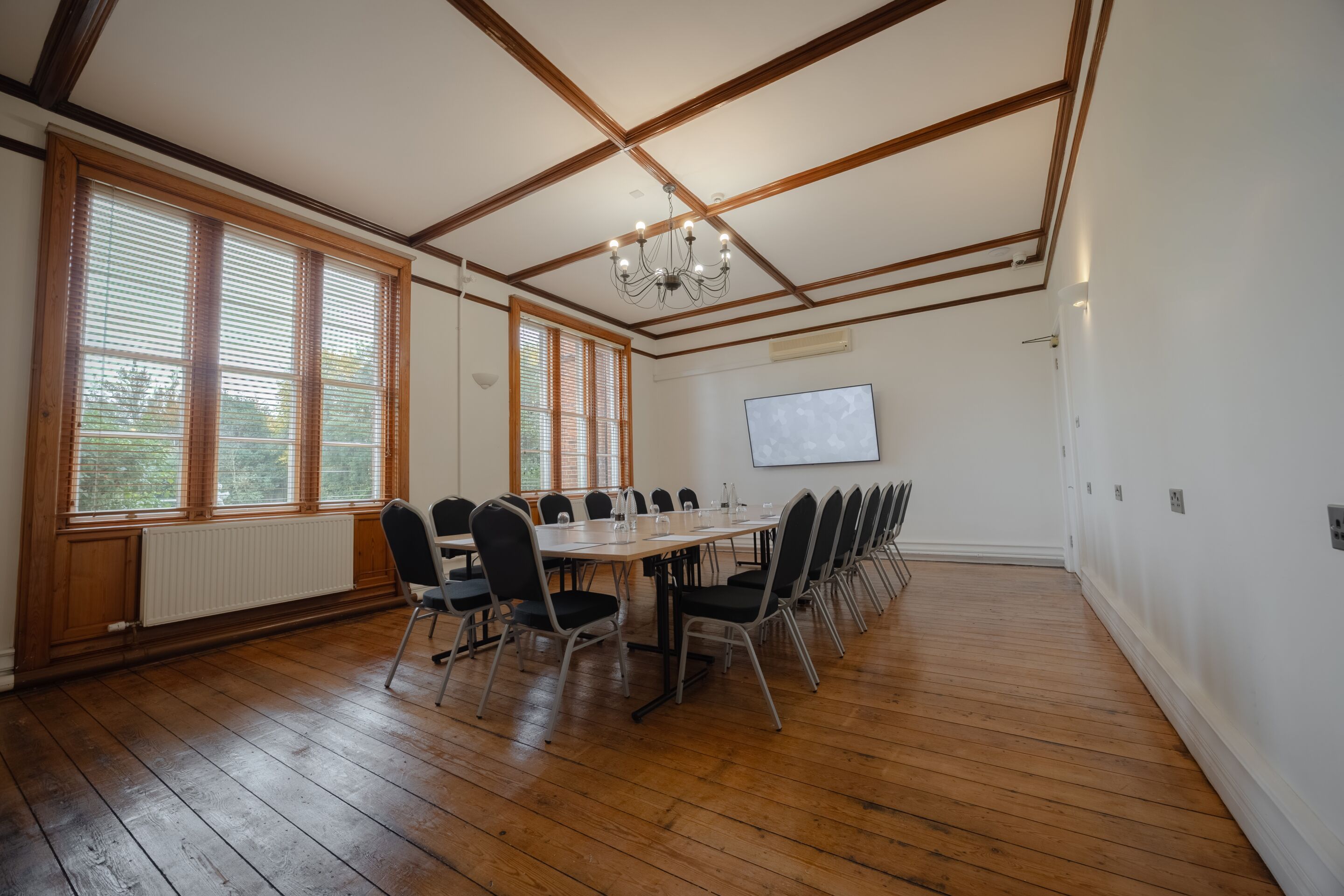Una sala de conferències amb una taula llarga, cadires, un lampadari, grans finestres i una pissarra blanca.