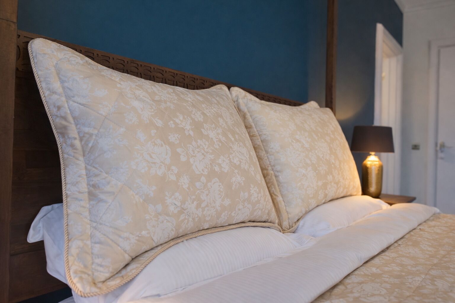 A bed with a headboard, a bedside lamp, and a wall with a door.