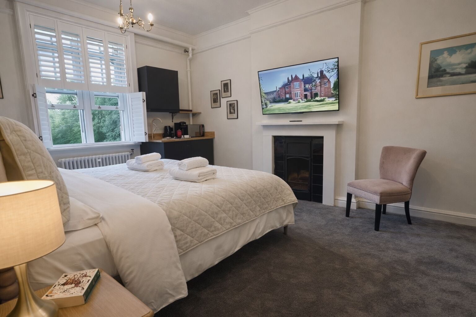 Habitación de hotel con una cama grande, un televisor sobre la chimenea, una silla y una ventana con persianas.