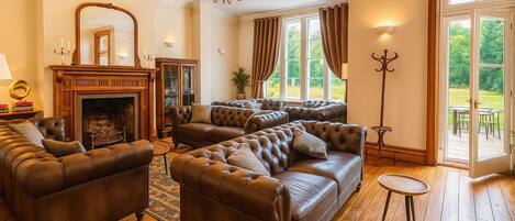 A spacious living room with leather sofas, a fireplace, and a large window with curtains.