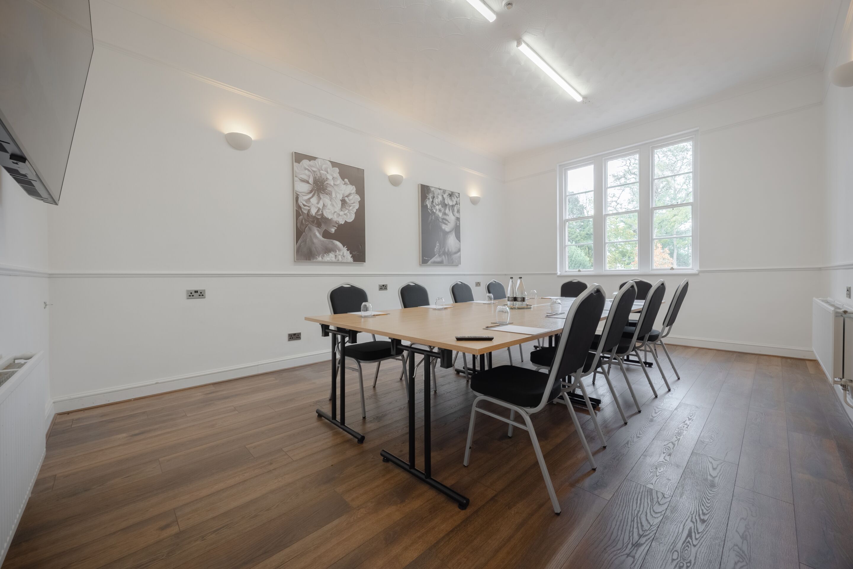 A conference room with a long table, black chairs, and two wall-mounted light fixtures.