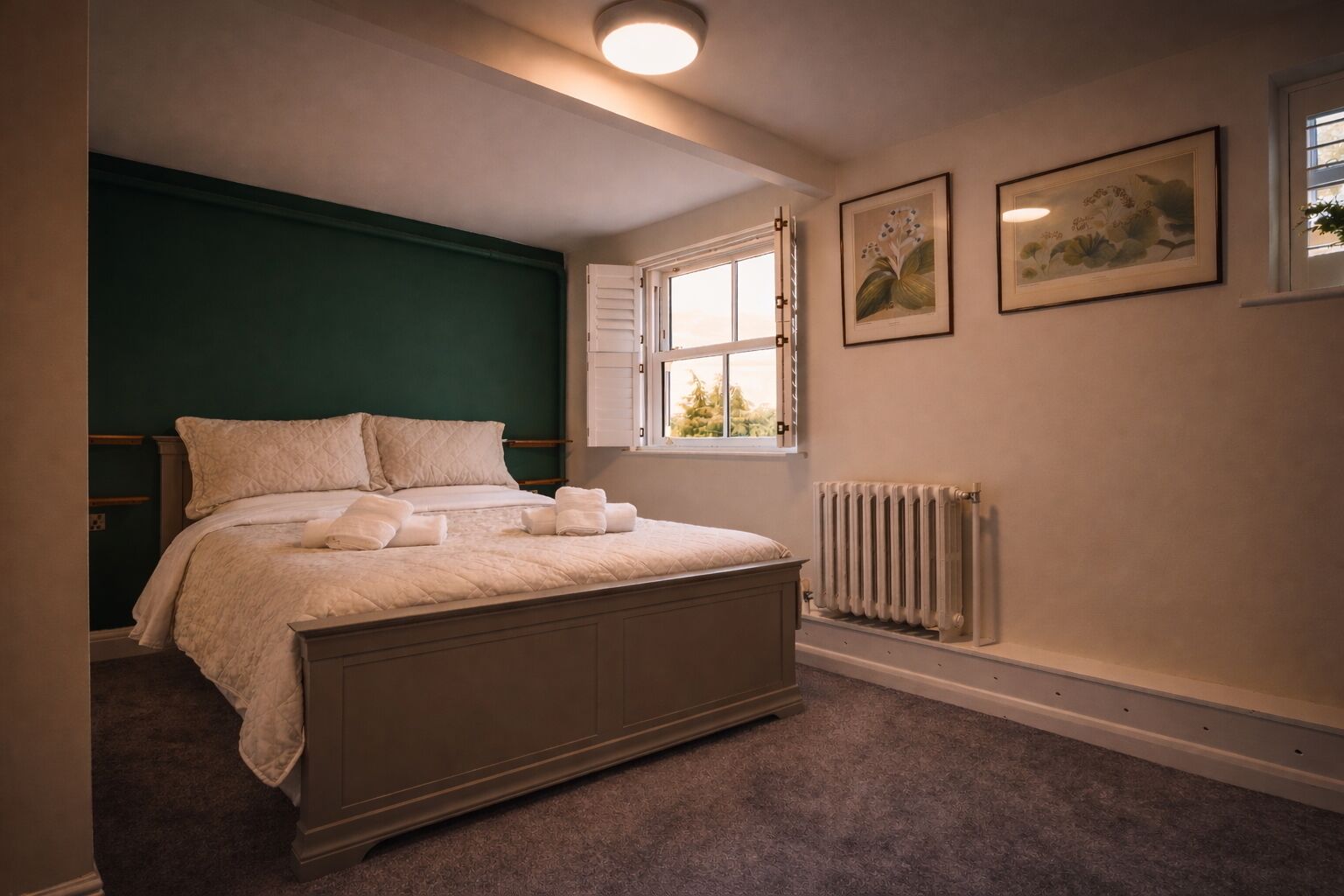 Un dormitorio con una cama, una ventana, un radiador y dos cuadros en la pared.