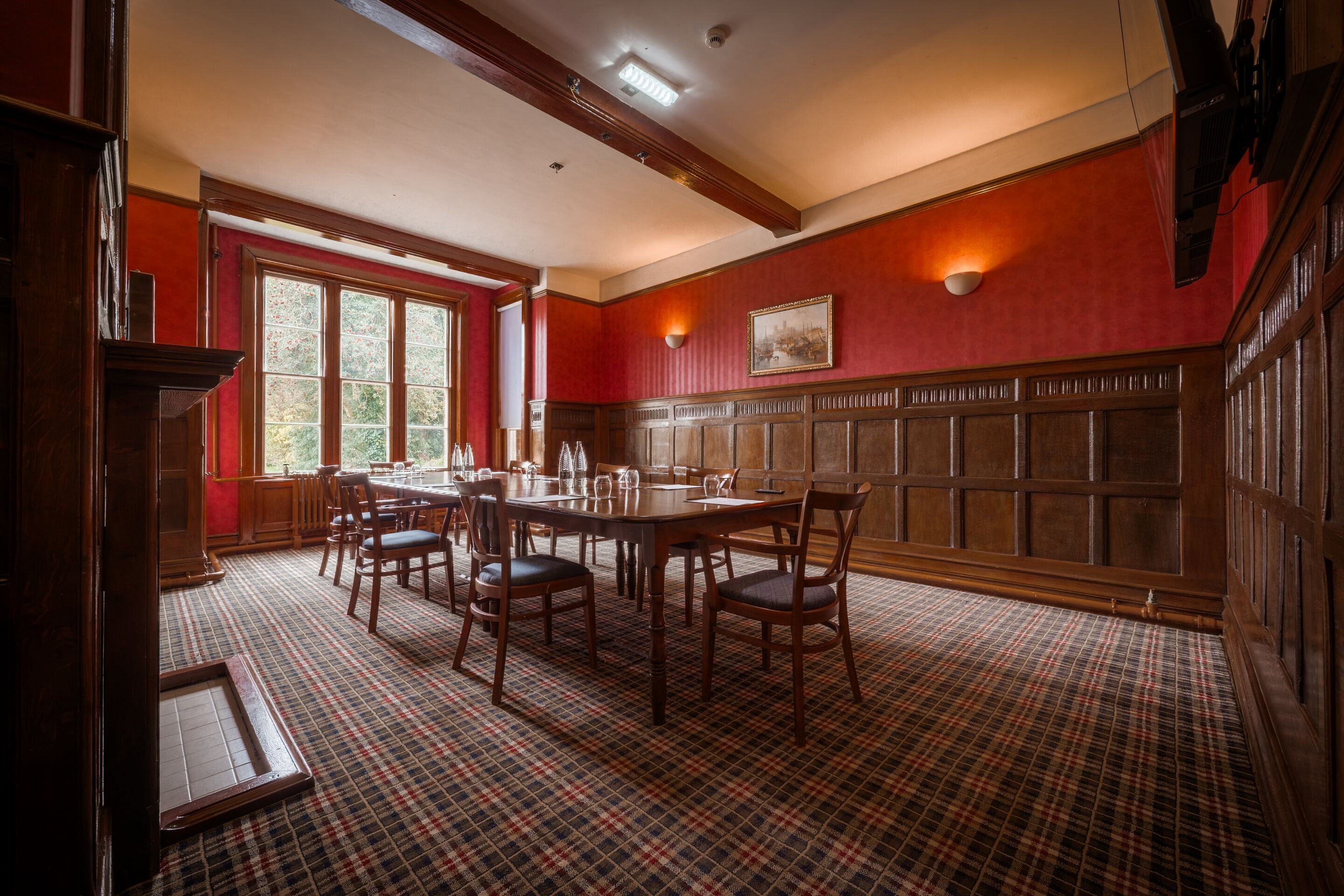 A dining room with a plaid carpet, wooden table, chairs, and a window with a view.