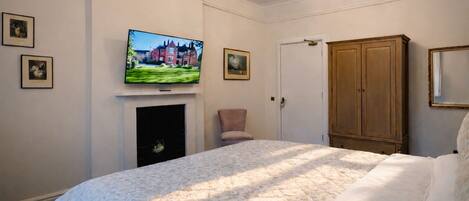 A bedroom with a bed, a television mounted above a fireplace, a wardrobe, and framed pictures on the wall.