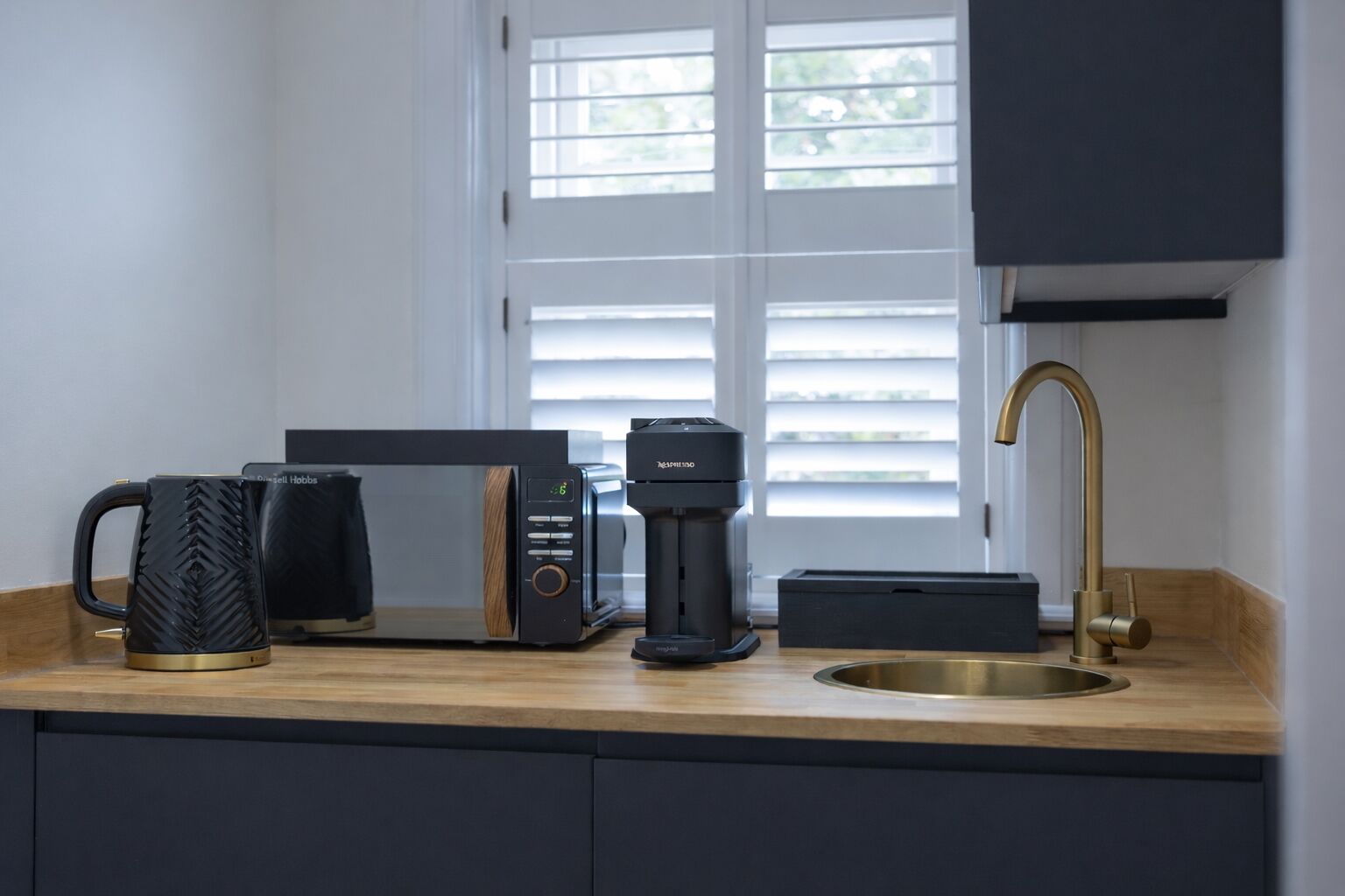 A kitchen with a coffee maker, a microwave, a coffee pot, and a sink.