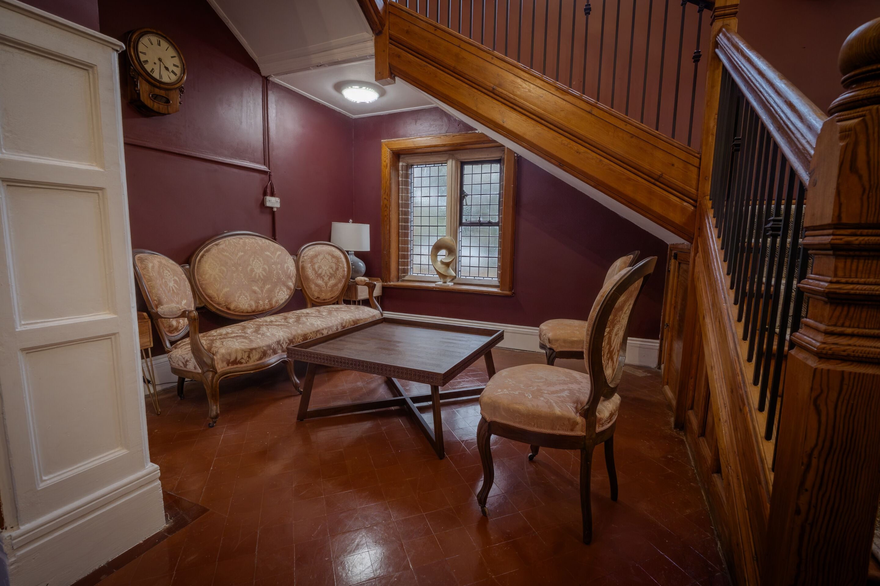 A room with a wooden staircase, a sofa set, a table, and a window with bars.