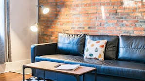 A modern living room with a blue leather sofa, a wooden coffee table, and a brick wall with hanging lights.
