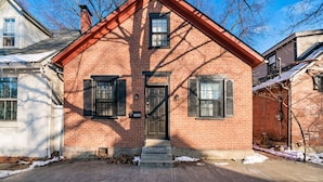 A red brick house with a front door, two windows with shutters, and a small porch.