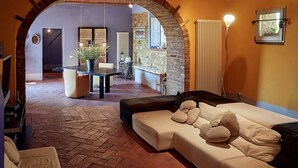 A cozy living area with a sofa, a coffee table, and a dining table. There is a stone wall and an archway leading to another room.