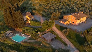 An aerial view of a property with a swimming pool, two main buildings, and surrounding greenery.