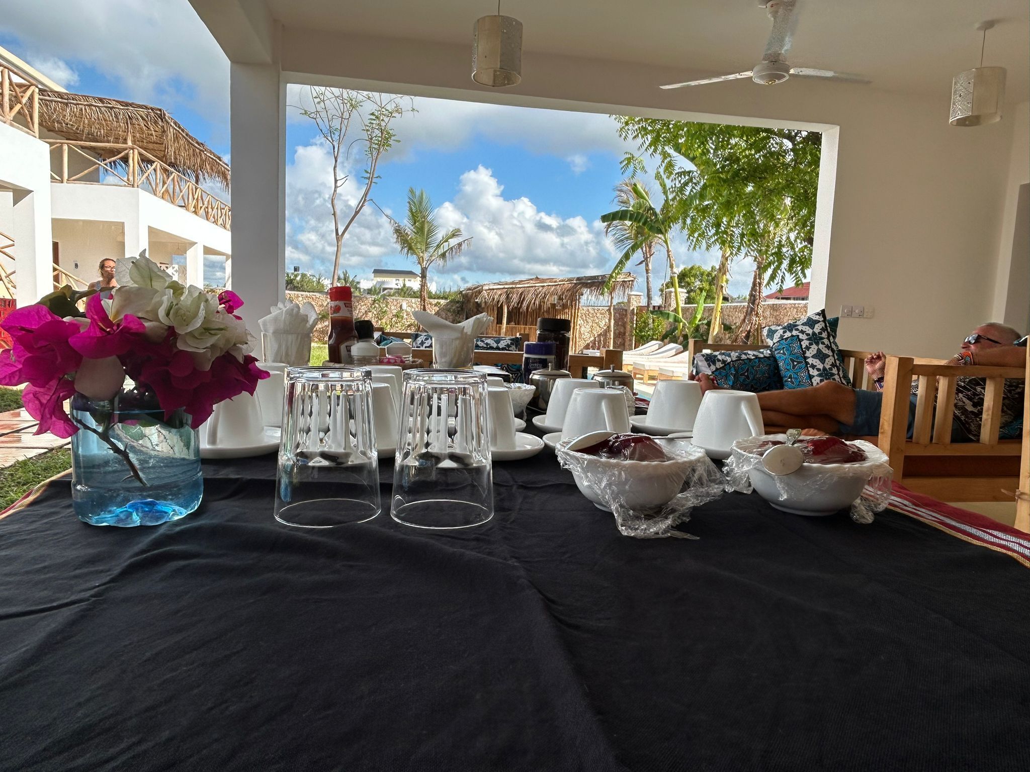 Mesa preparada para una comida con vistas a un paisaje tropical, con palmeras y una estructura de techo de paja.