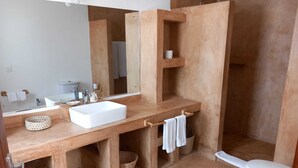 Een badkamer met een houten wastafelmeubel, een witte wastafel, een spiegel, een handdoekrek en een toilet.