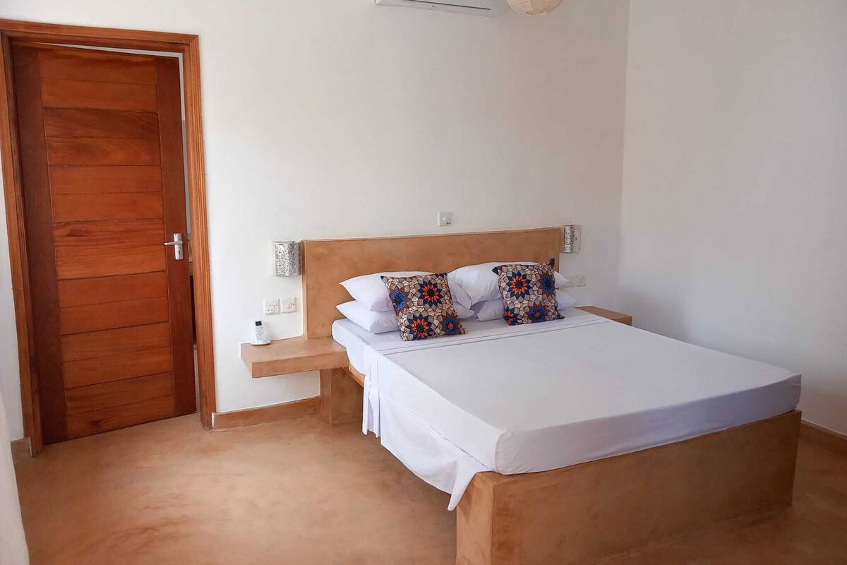 Ein Schlafzimmer mit einem hölzernen Bett, weißer Bettwäsche und gemusterten Kissen.