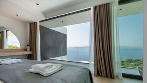 A modern hotel room with a large bed, a view of the sea, and a balcony with curtains. - Villa Brela-Rogac 3 (Baska Voda)