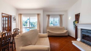 A living room with a sofa, a dining table with chairs, a fireplace, and large windows with curtains. - Villa Gabriella - Charming villa in great location (Guia)