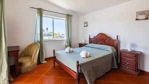 A bedroom with a wooden bed, a chair, a nightstand, and a window with curtains. - Villa Gabriella - Charming villa in great location (Guia)