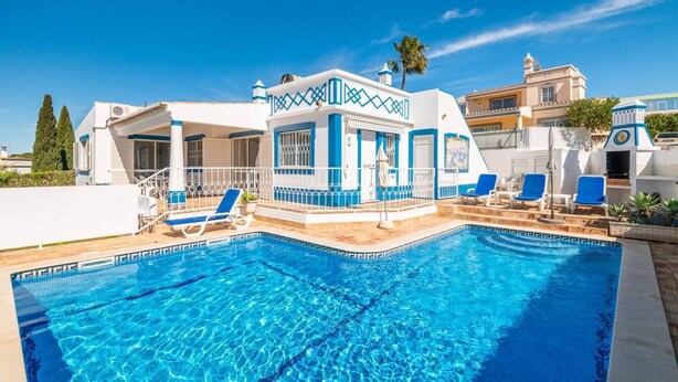 A swimming pool with blue water, surrounded by lounge chairs and a building with blue and white exterior. - Villa Gabriella - Charming villa in great location (Guia)