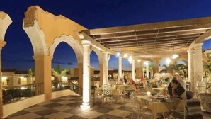 An outdoor dining area with checkered flooring, white columns, and tables with chairs.