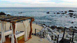 A beachside cabana with a wooden roof and white curtains, overlooking the ocean.