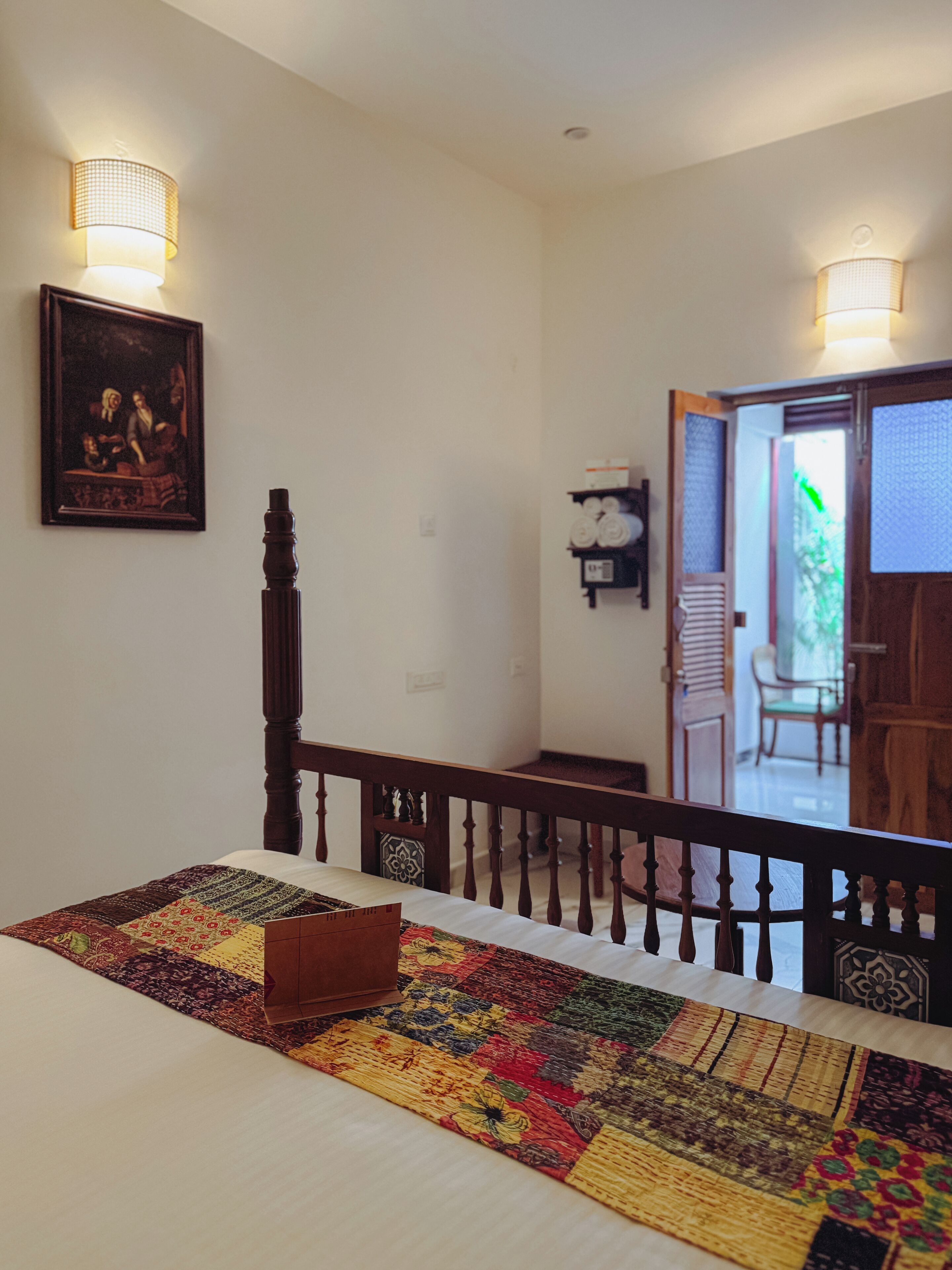 A bedroom with a wooden bed, a colorful quilt, and a painting on the wall.